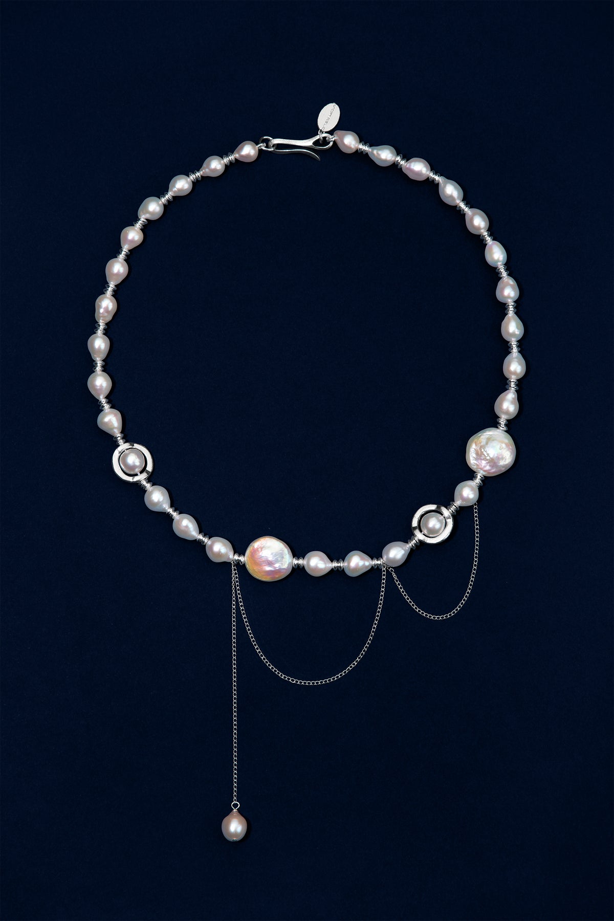 A sterling silver necklace featuring baroque pearls in white and iridescent tones, accented with sterling silver rings and chains, displayed on a dark navy blue background.