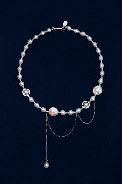 A sterling silver necklace featuring baroque pearls in white and iridescent tones, accented with sterling silver rings and chains, displayed on a dark navy blue background.