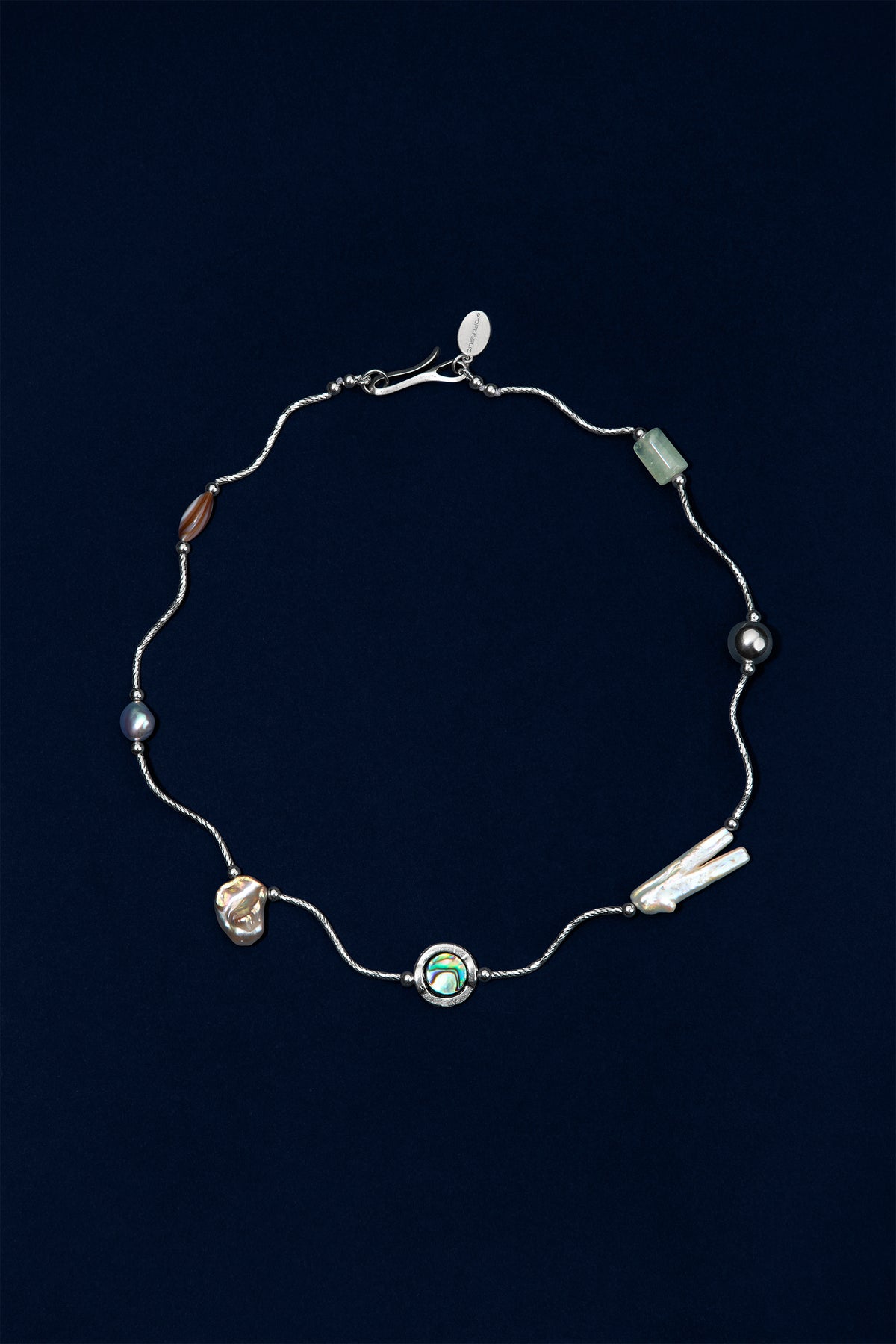 A delicate sterling silver wave necklace with multiple small pearl and stone accents in various colors, including a central abalone shell displayed on a dark navy blue background.