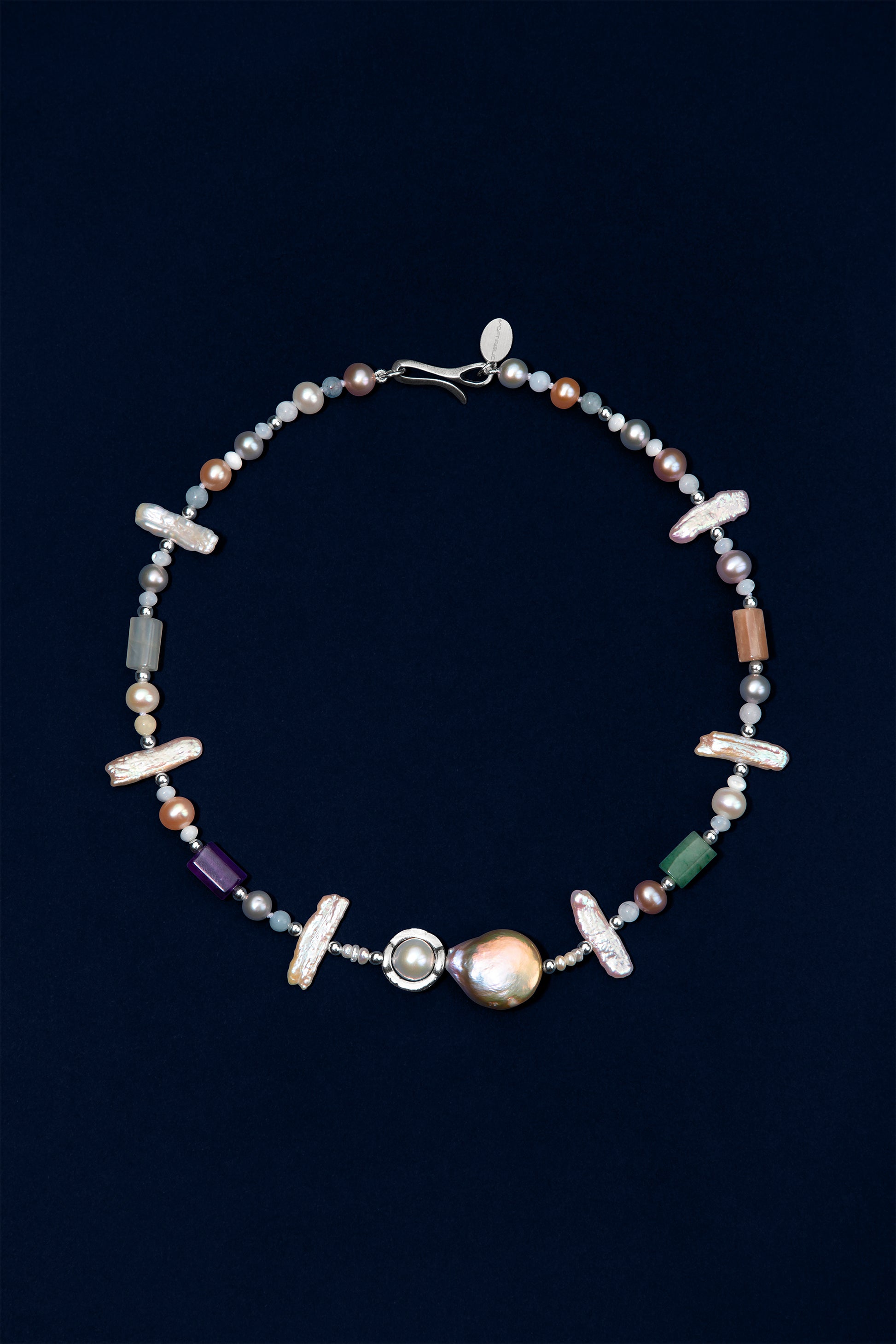 A beaded necklace featuring a large iridescent pearl, silver-toned beads, small multicolored pearls, white stick pearls, and semi-precious stones displayed on a dark navy background.